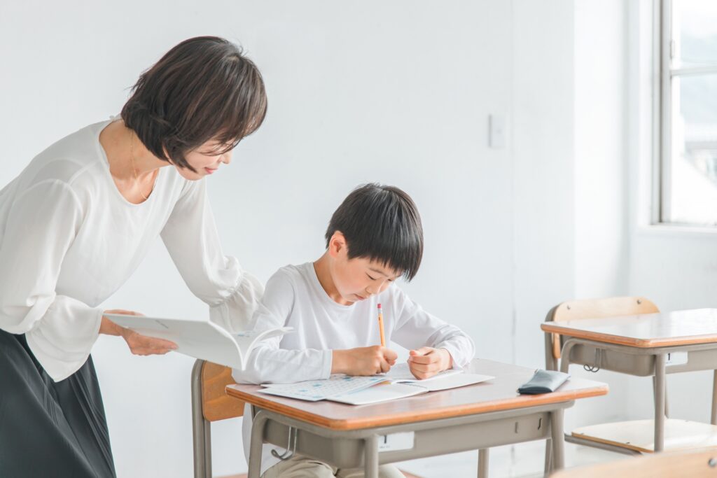 鉛筆を持って勉強をしている男の子とそれに本を持ちながら教えている女性教員